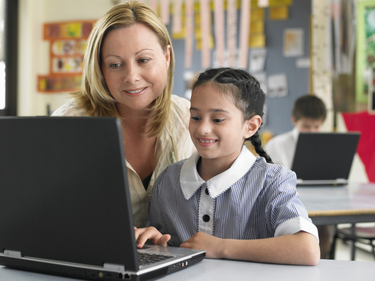 Teacher assistant and primary school student using a laptop inside an Australian classroom.