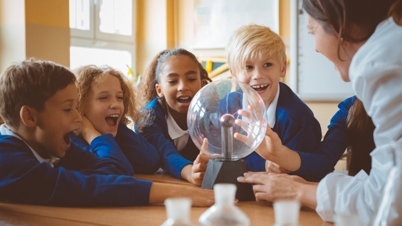 Small group of student and a teacher aide enjoying a science experiment in a classroom environment.