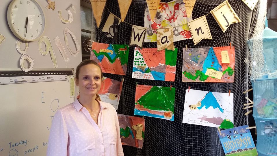 Learning Support Officer Stands in front of colourful work samples made by students.