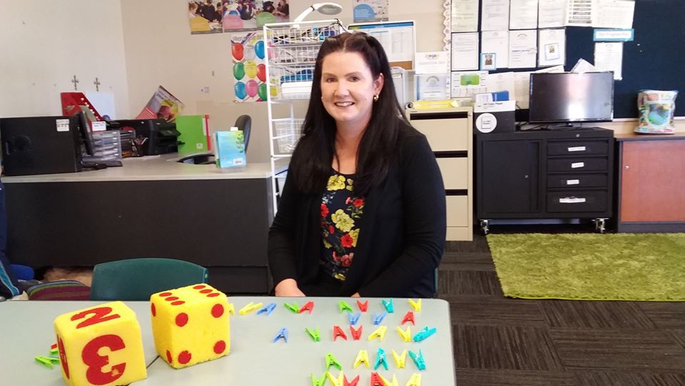 Female LSO sits at desk with equipment for learning including pegs and toys.