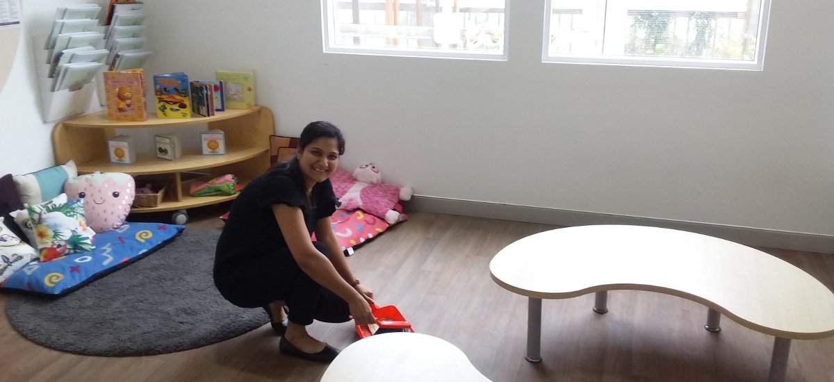 Female teacher aide with dust pan and shovel doing light cleaning in classroom.