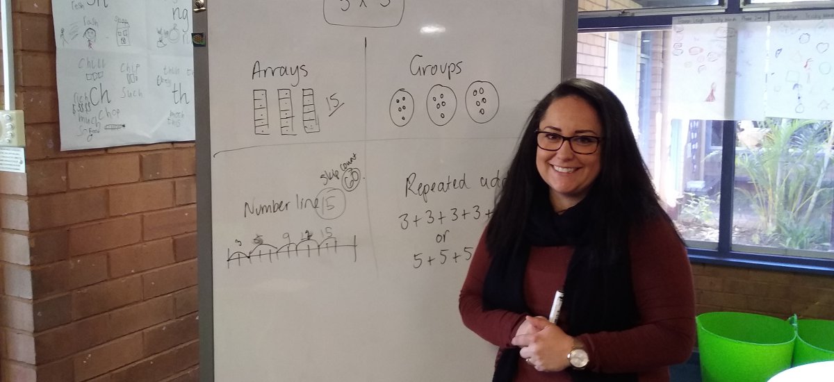 Female SSO in front of white board which has maths problems ready for students.