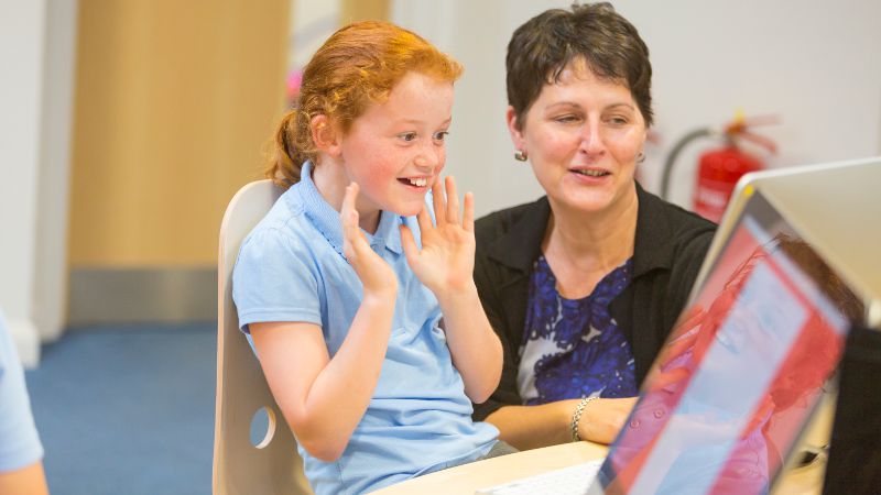 Teacher assistant supporting a student on a computer.