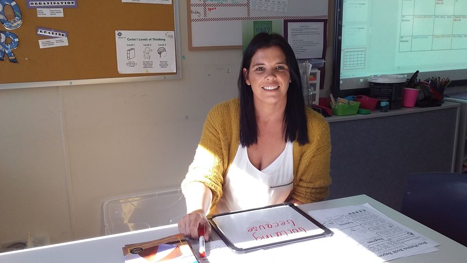 Teacher aide sitting at desk in a classroom setting.