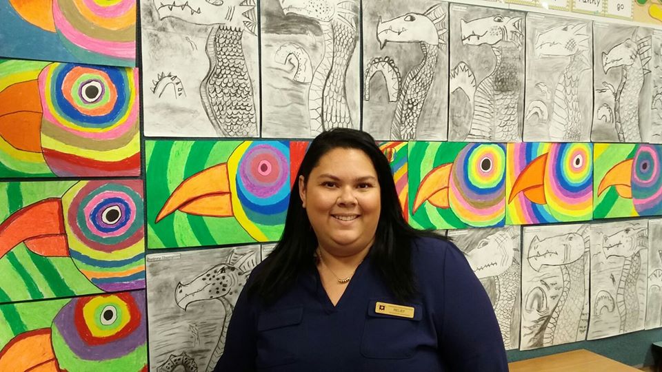 A image of a teacher aide standing in front of school artwork.
