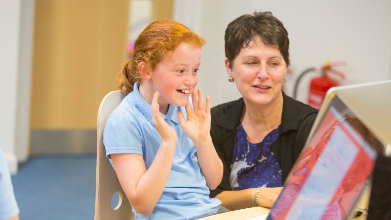 Teacher aide supporting a student and teacher in a classroom environment.