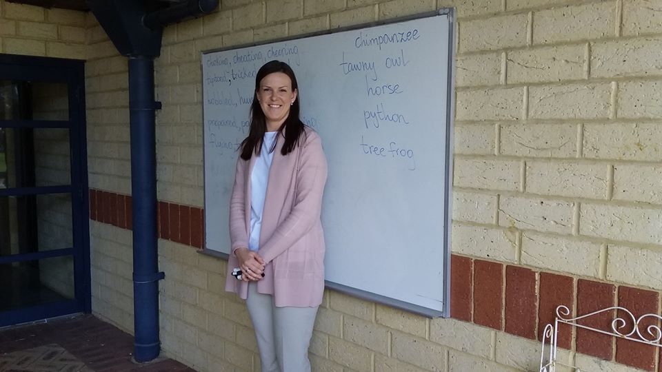Teacher aide standing infront of a whiteboard in a school classroom.