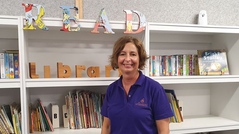 A image of a teacher aide standing in a small school library.