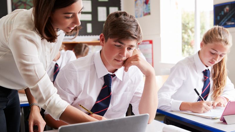 Teacher assistant working with senior students in a classroom.