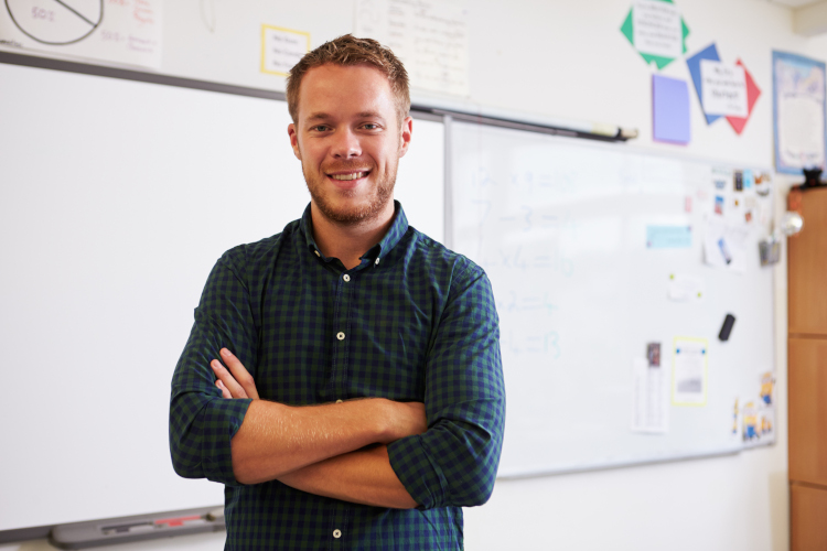 Smiling teacher aide standing infront of a whiteobard in a classroom setting.