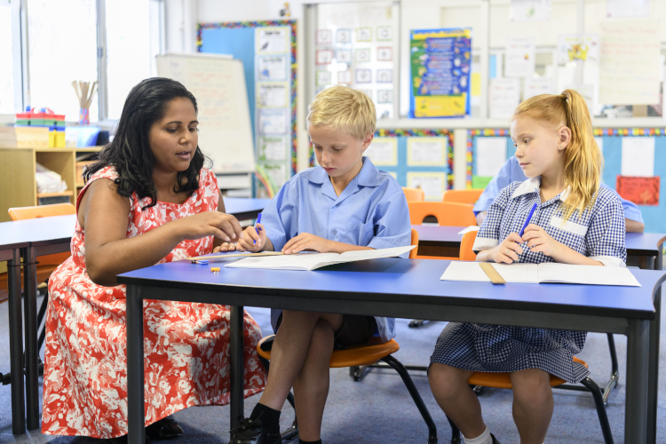 Teacher assistant working with two students in a primary school classroom.