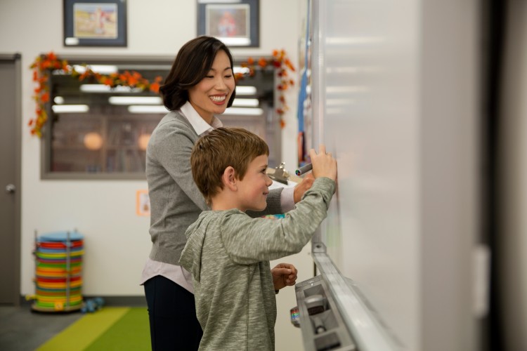 Teacher aide and young boy writing on white board