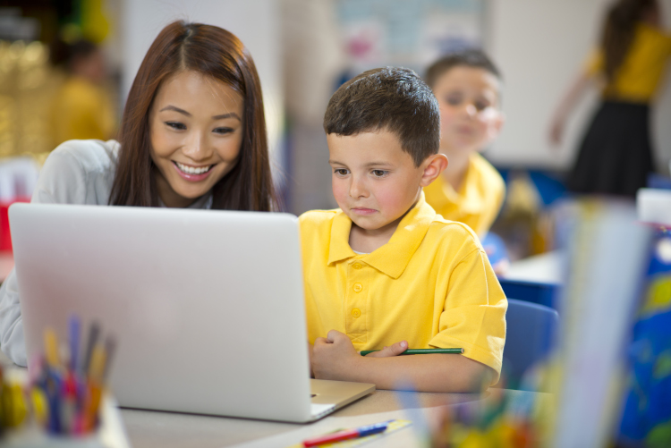 Teacher aide and primary school student using a laptop.